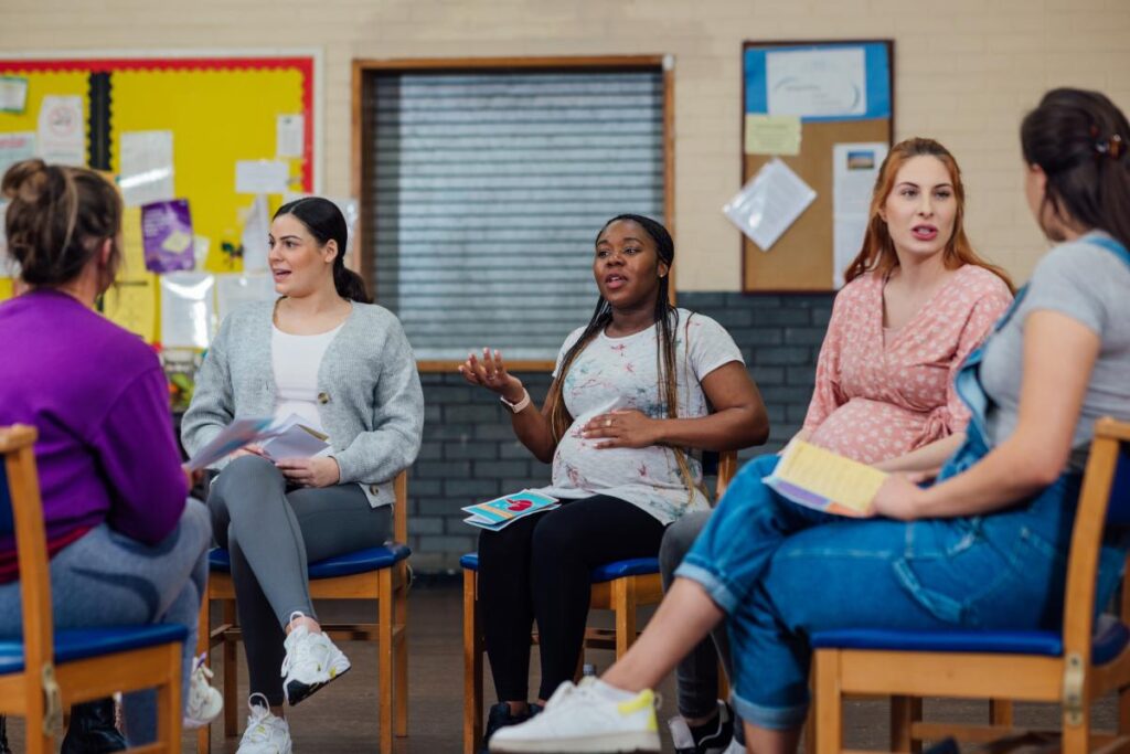 An over the shoulder view of a group of pregnant women who are sharing their journey together. They are attending a pregnancy group and fitness class in a community centre